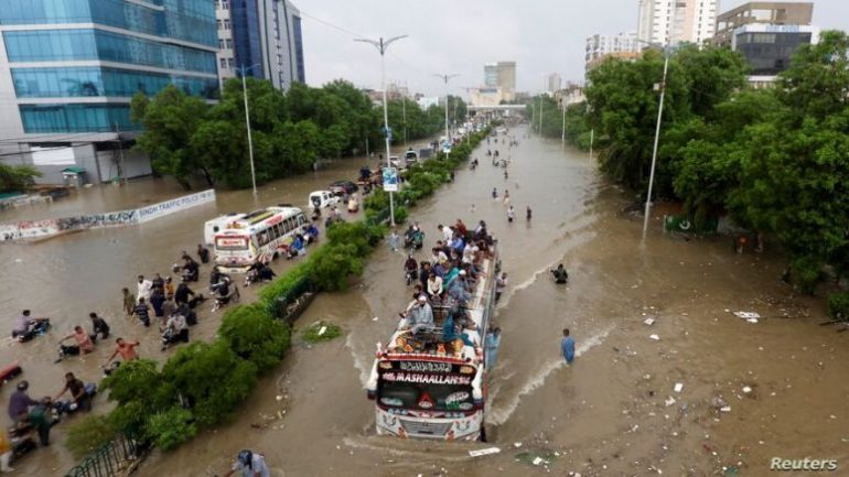 کراچی، پانی میں ڈوبی بس پر مسافر چڑھے ہوئے ہیں