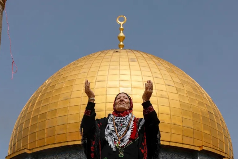 ایک فلسطینی بزرگ خاتون قبتہ الصخرا کے سامنے دعا کے لیے ہاتھ پھیلائے ہوئے